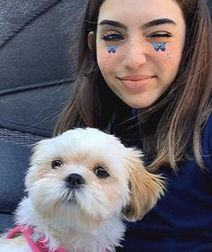 a woman with blue butterflies painted on her face sitting next to a small white dog