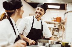 a man and woman are smiling while cooking in a commercial kitchen with pots on the stove