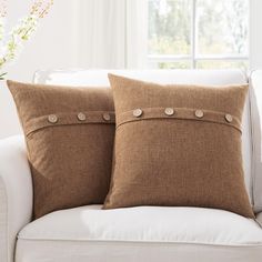 two brown pillows sitting on top of a white couch next to a vase with flowers