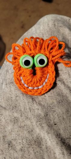 an orange crocheted monster brooch with googly eyes