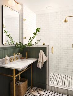 a white tiled bathroom with black and white tile flooring, gold faucet, brass fixtures and green accents