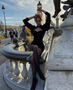 a woman sitting on top of a stone bench next to a lamp post and statue