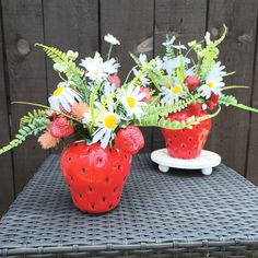 two strawberry shaped vases filled with flowers on top of a table next to a wooden fence