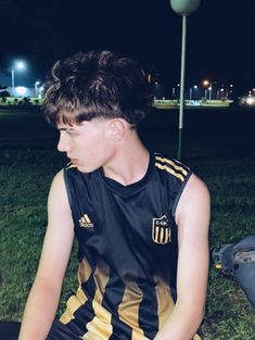 a young man sitting on the ground wearing a black and yellow shirt with gold stripes