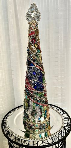 a multi - colored christmas tree made out of jewelry sits on a round table in front of a white curtain