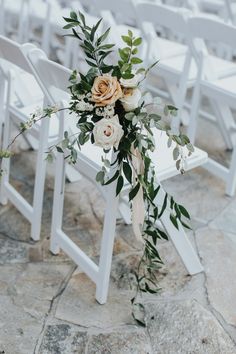 an arrangement of flowers and greenery sits on the back of a white folding chair