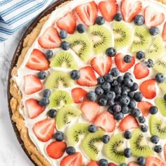 a pie topped with sliced kiwis, strawberries and blueberries on top