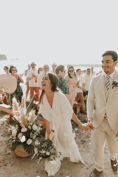 a bride and groom walking down the beach with their wedding party in the back ground