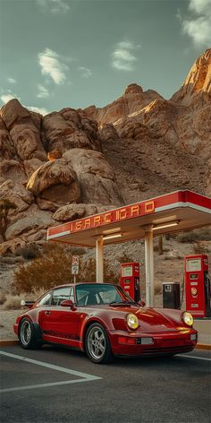 a red sports car parked in front of a gas station with mountains in the background