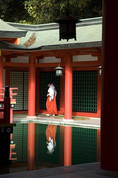 a person in an orange outfit standing by a pool with red pillars and green doors