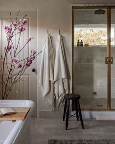 a white bath tub sitting next to a wooden stool in a bathroom under a window