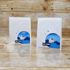 two white cards with blue waves on them sitting on top of a wooden table next to each other