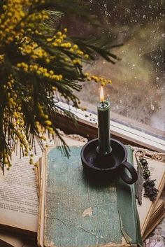 an open book with a candle on top of it next to a window sill