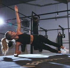 a woman is doing push ups on the ground in a gym with punching bags behind her