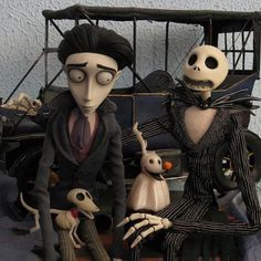 two figurines sitting next to each other in front of a car with skeletons on it