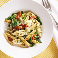 a white bowl filled with pasta and spinach on top of a yellow place mat