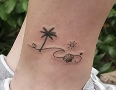 a woman's foot with a small palm tree and seashell tattoo on it