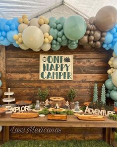 a table topped with lots of balloons next to a sign that says one happy camper