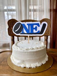 a white cake sitting on top of a wooden table next to a sign that says one