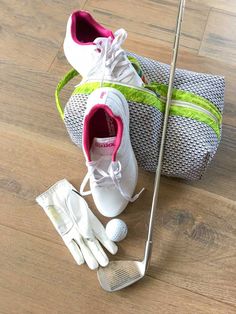 a pair of white shoes and golf clubs on a wooden floor next to a bag