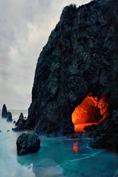 an orange light in the middle of a cave near some water and rocks on a cloudy day