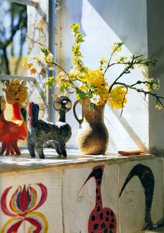 vases with flowers and figurines are sitting on a window sill in the sun