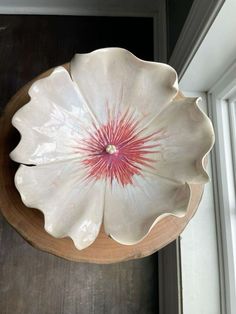 a white flower shaped bowl sitting on top of a wooden table next to a window