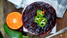 a bowl filled with cranberry sauce next to an orange