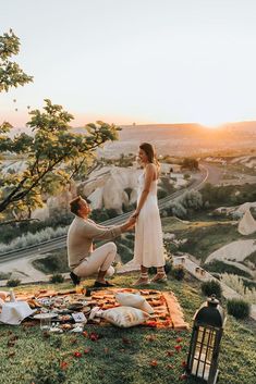 a man and woman sitting on top of a grass covered hill