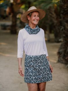 an older woman in a hat and dress smiles at the camera while standing on a dirt road