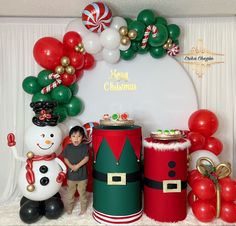 a child standing in front of some christmas decorations and balloon arch with snowman, santa clause, candy canes