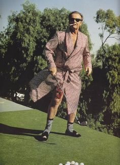 a man in a robe is playing golf on the green with white balls behind him