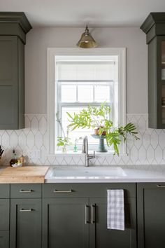 a kitchen with green cabinets and a white tile backsplash that has a potted plant on the window sill