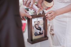 a man and woman holding a framed photo in front of their wedding guests'hands