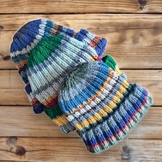 two knitted hats sitting on top of a wooden table next to each other and one is multicolored