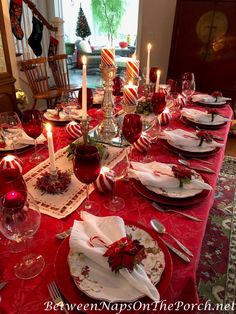 a table set for christmas dinner with red and white plates, silverware and candles