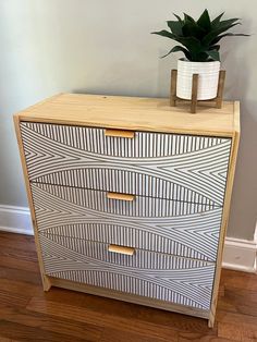 a wooden dresser with two drawers and a potted plant sitting on top of it