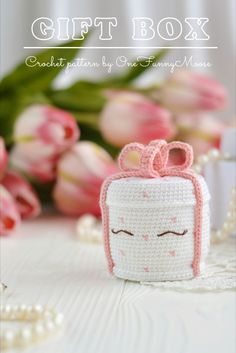 a small crocheted box with a bow on it sitting next to pink flowers