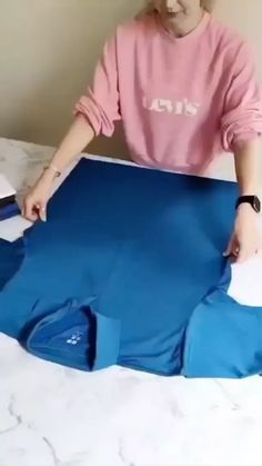 a woman in pink shirt cutting blue material on top of a white sheeted bed