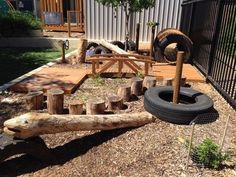 an outdoor play area made out of tree trunks and logs with a tire on the ground