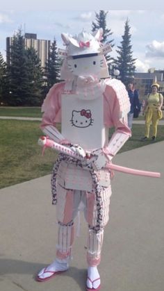 an inflatable hello kitty costume is standing on the sidewalk while holding a pink stick