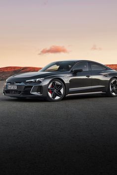 a grey sports car parked on the side of a road at sunset with mountains in the background