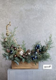 an arrangement of evergreen, pine cones and berries in a wooden box with a gold ornament