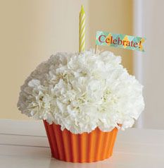 a cupcake decorated with white flowers and a birthday candle is sitting on a table