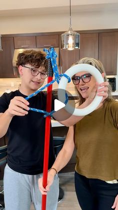 a man and woman standing in a kitchen holding up an object with blue string attached to it