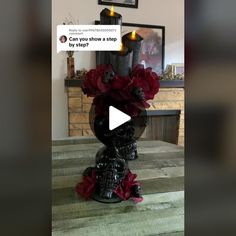 a black vase with red flowers in it sitting on top of a wooden table next to a fireplace