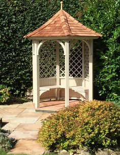 a white gazebo sitting in the middle of a garden next to bushes and shrubbery