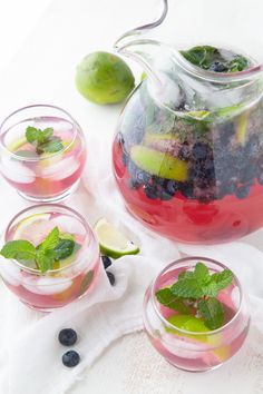 three glasses filled with fruit and ice on top of a white cloth next to a pitcher