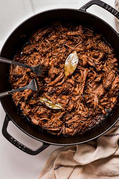 a pot full of pulled pork on top of a white table with a spoon in it