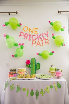 a table topped with cakes and desserts next to a cactus wall hanging from the ceiling